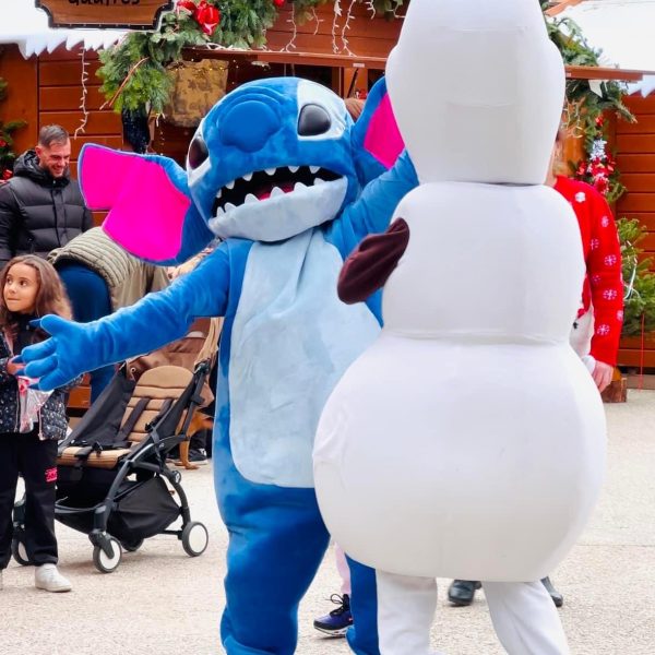 Stitch et Olaf dansant joyeusement ensemble. Stitch, avec sa fourrure bleue, et Olaf, le bonhomme de neige joyeux de Frozen, partagent un moment ludique sur une scène ou un espace festif.